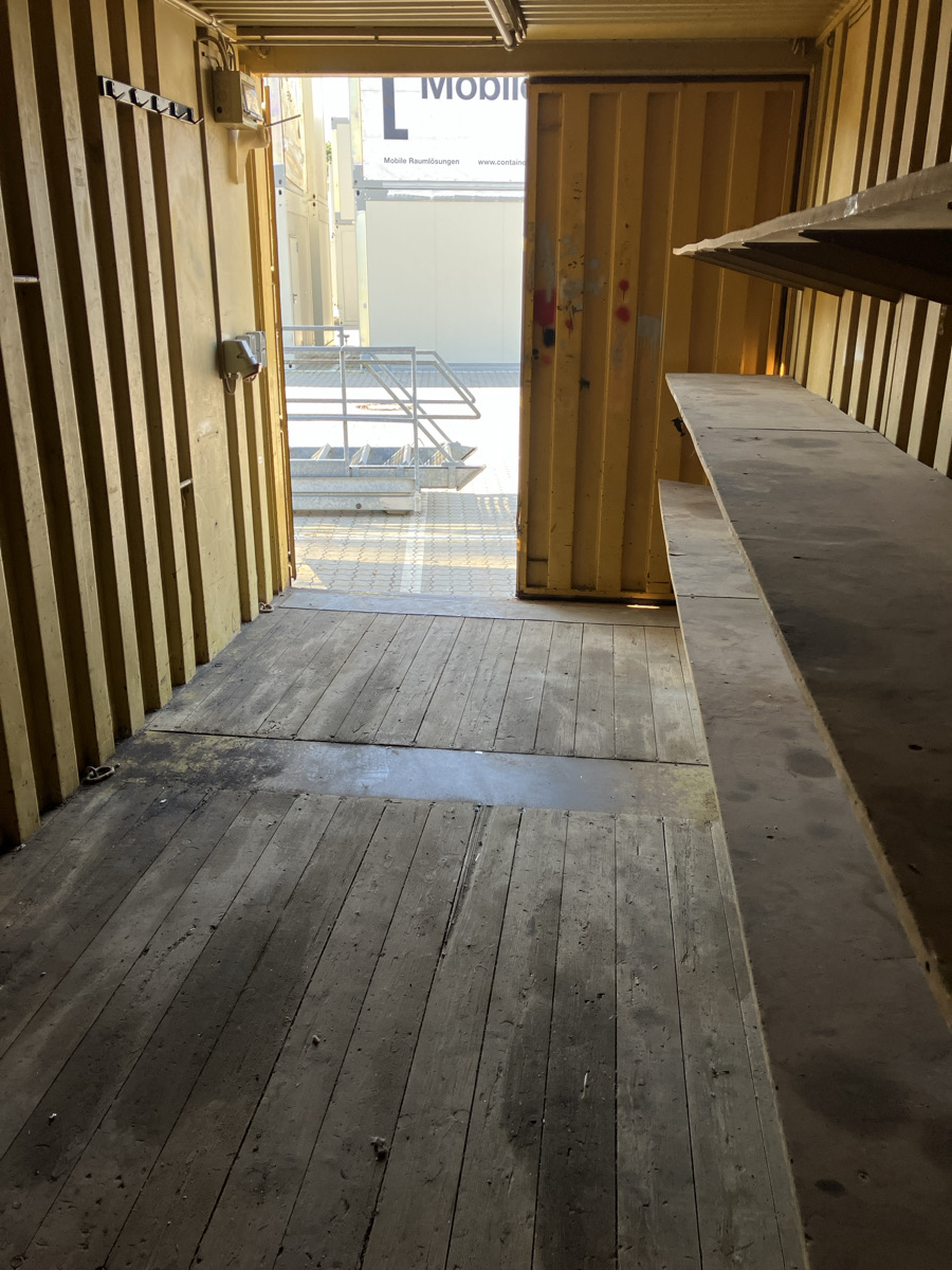 Innenansicht eines gebrauchten gelben Containers mit Holzboden, Regal und geöffneter Tür