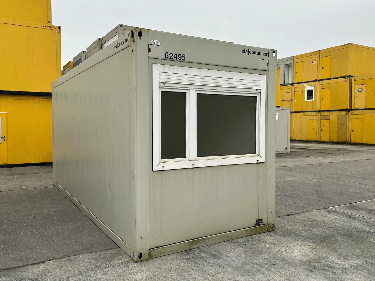 Außenansicht eines gebrauchten grauen Bürocontainers mit Fenster und Rollladen auf einem Betriebsgelände.