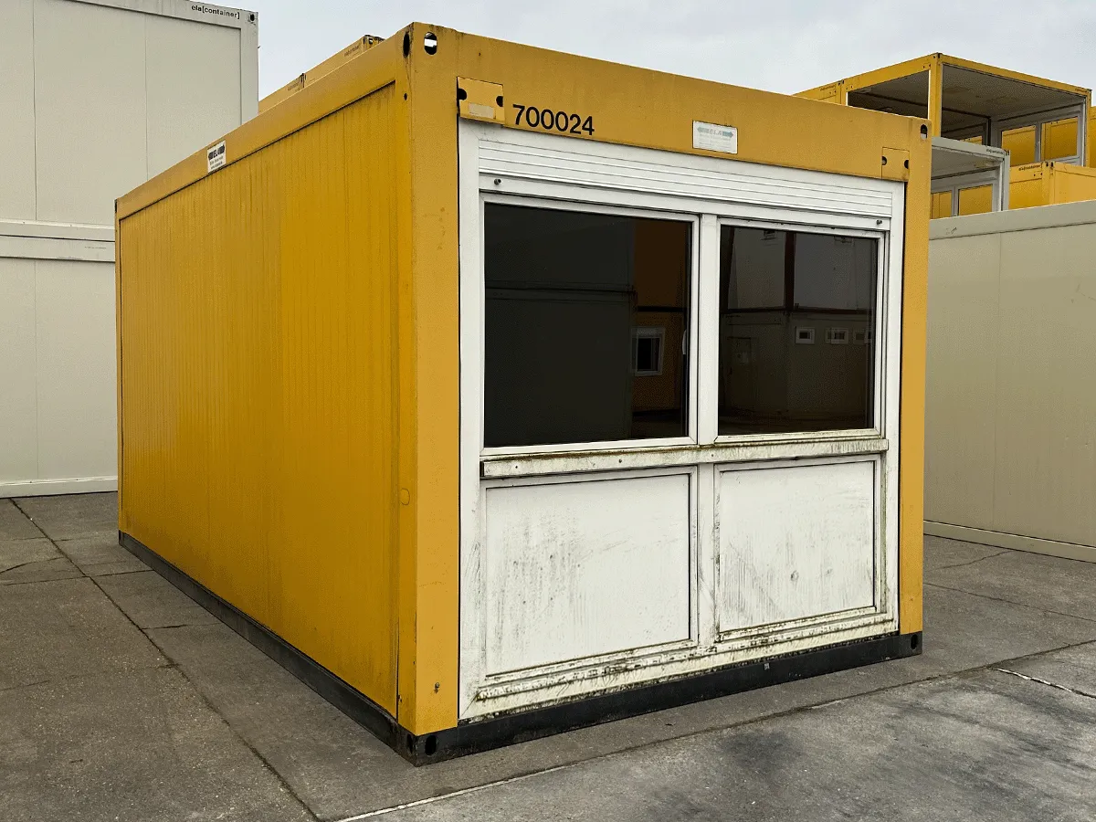 Außenansicht eines gebrauchten grauen Bürocontainers mit Fenster und Rollladen auf einem asphaltierten Platz.