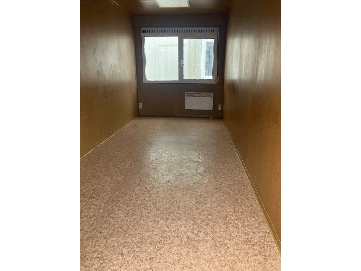 Innenansicht eines leeren gelben Bürocontainers mit Blick auf das Doppel-Fenster, den Heizkörper und hellen Bodenbelag.