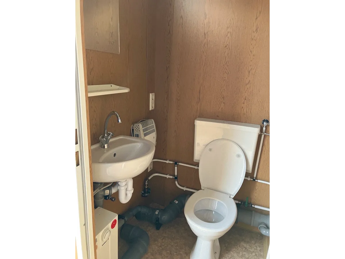Sanitärbereich im Container mit WC, Waschbecken, Spiegel und sichtbarer Rohrinstallation