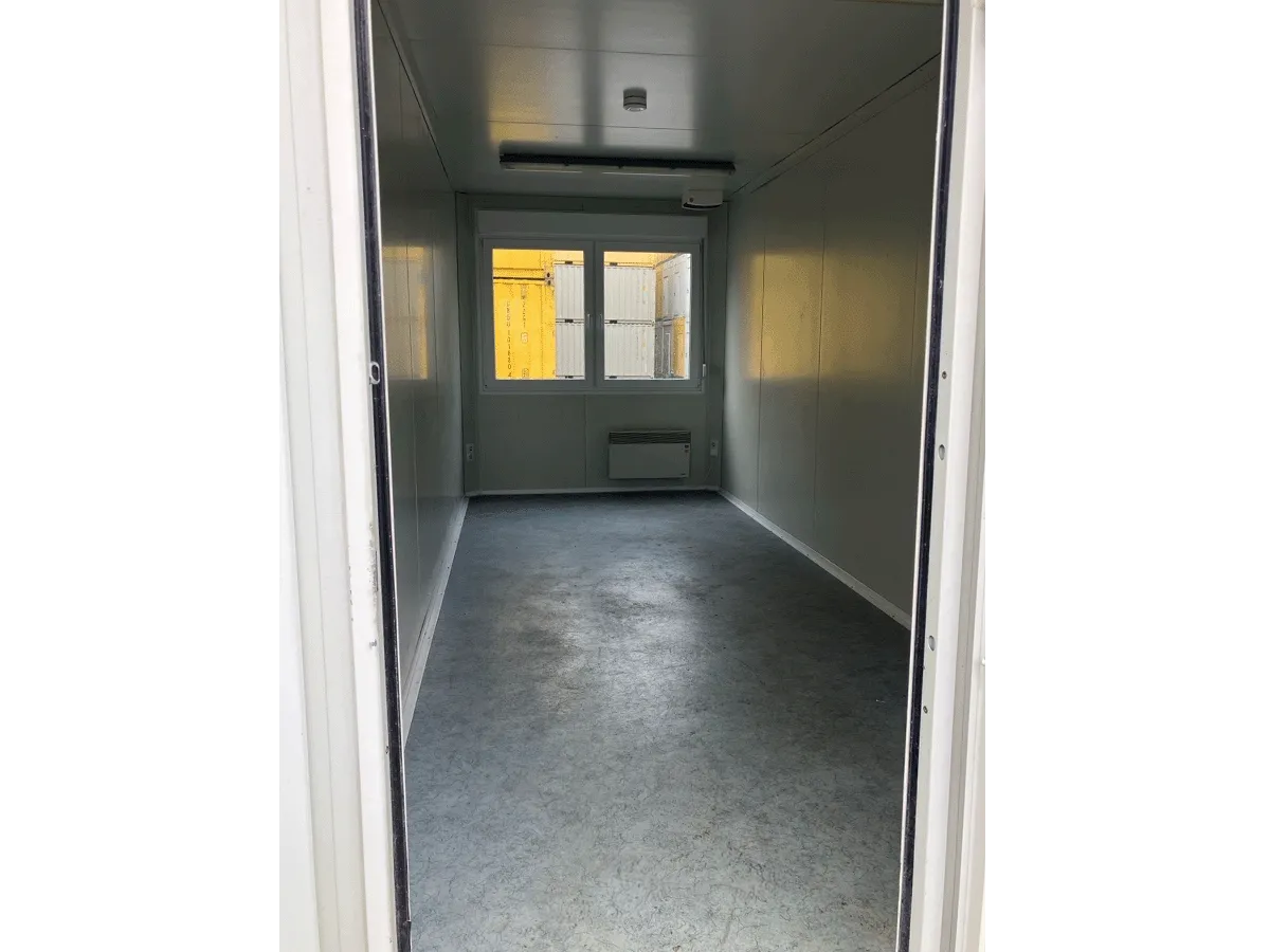 Innenansicht eines gebrauchten grauen Bürocontainers mit Fenster, Heizkörper und grauem Bodenbelag.