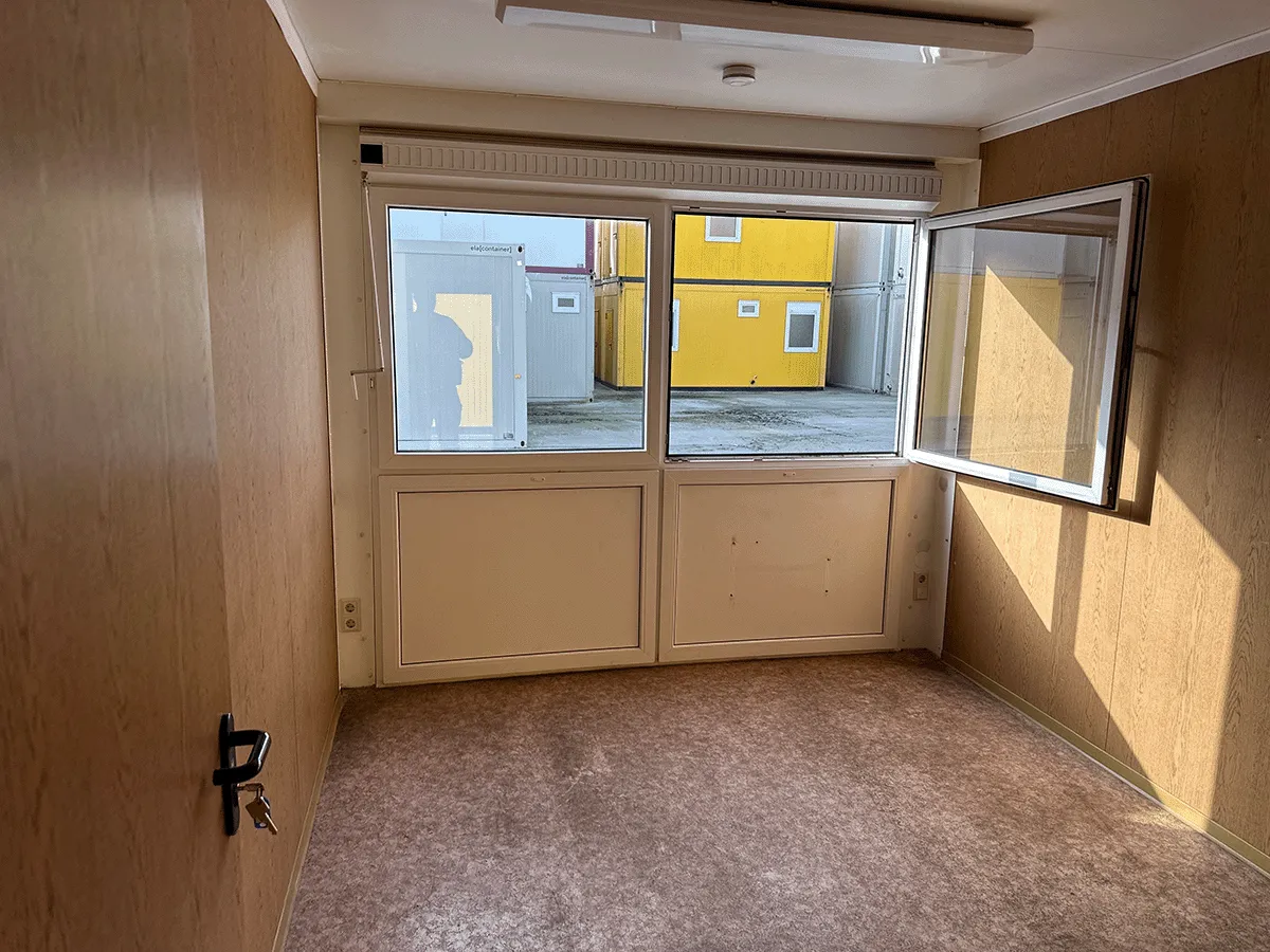 Innenansicht eines gelben Bürocontainers mit Blick auf die geschlossene weiße Eingangstür und den Sicherungskasten.