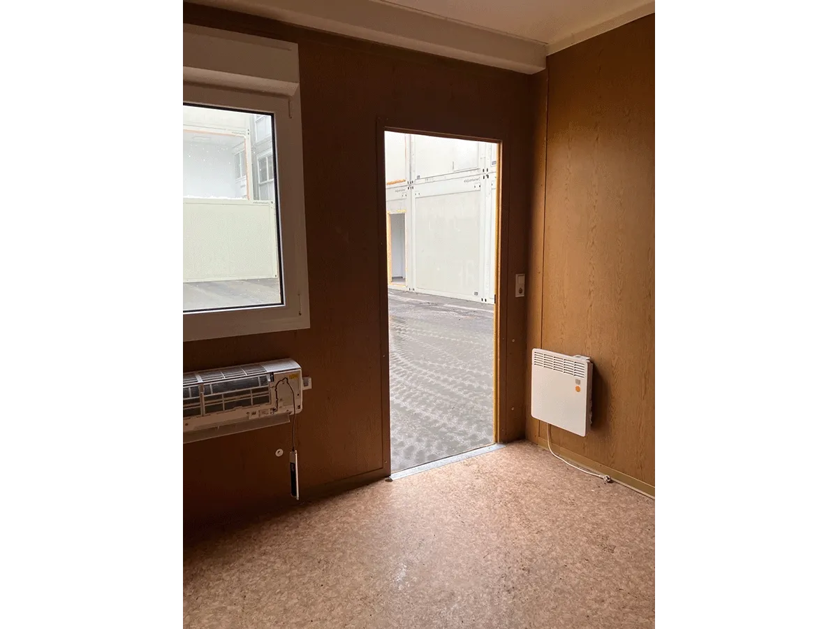 Gebrauchter 20 Fuß Bürocontainer Innenansicht mit Glastür, Heizkörper und Bewegungsmelder – Blick Richtung Eingang