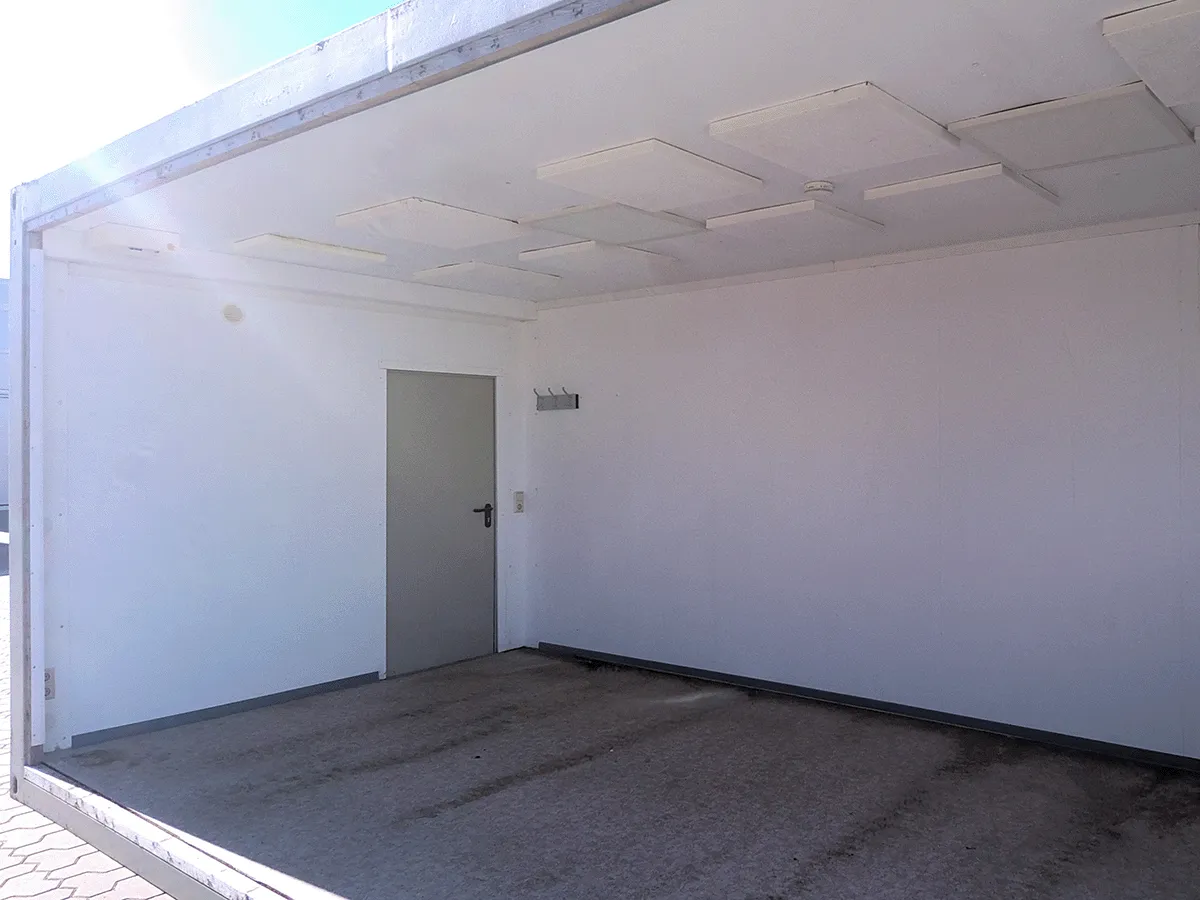 Innenansicht eines grauen 20 Fuß Bürocontainers (3m Breite) mit Blick auf die geschlossene graue Eingangstür und Deckenbeleuchtung.
