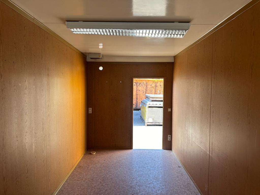 Gebrauchter Bürocontainer Innenraum mit Holzpaneelen Deckenbeleuchtung und offener Eingangstür