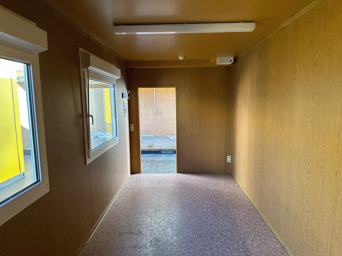 Gebrauchter 20 Fuß Bürocontainer Innenansicht mit zwei Fenstern, offener Eingangstür und Deckenbeleuchtung – Blick zum Ausgang
