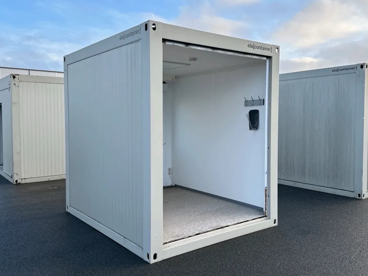 Innenansicht eines leeren grauen Bürocontainers mit Fenster, Heizkörper und hellem Bodenbelag.