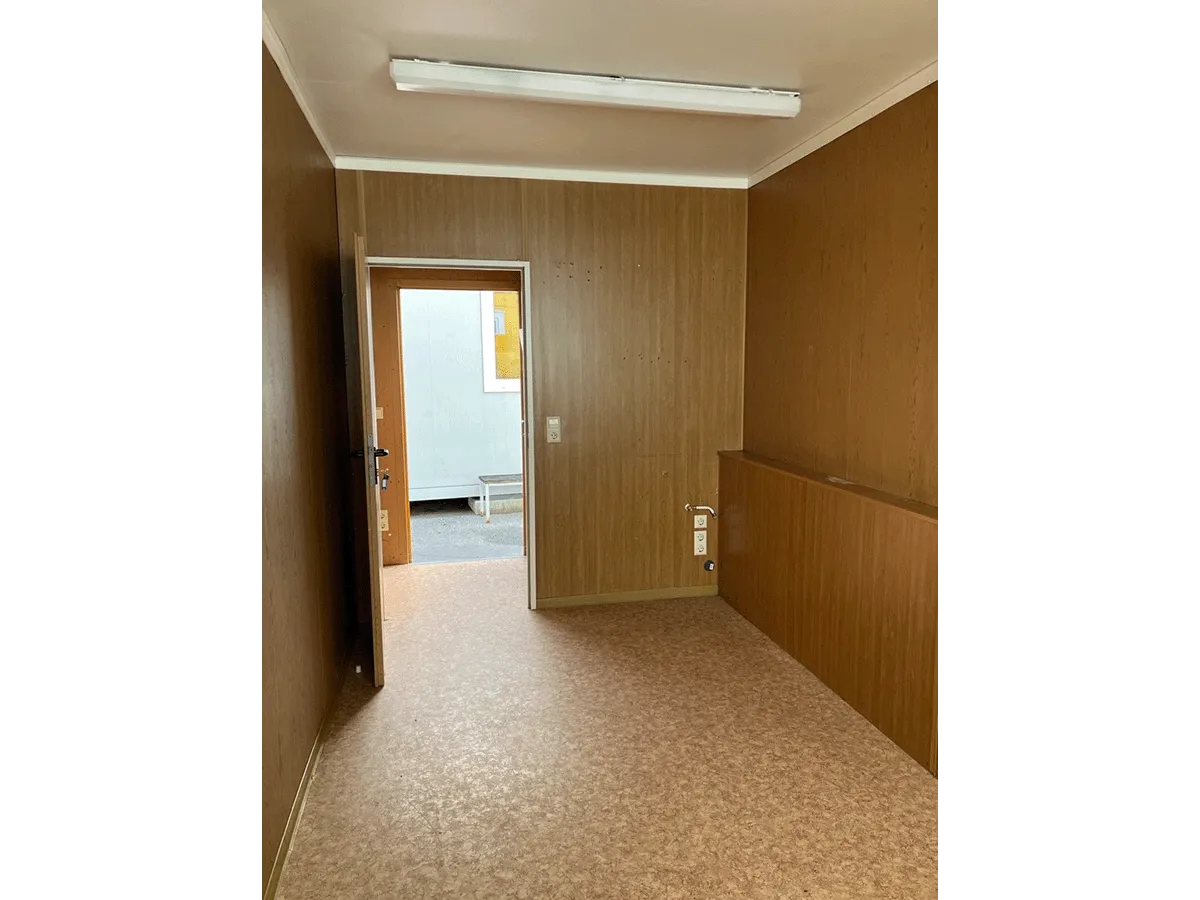Innenansicht leerer Bürocontainer mit Holzwand-Dekor, Linoleumboden und Leuchtstoffröhre