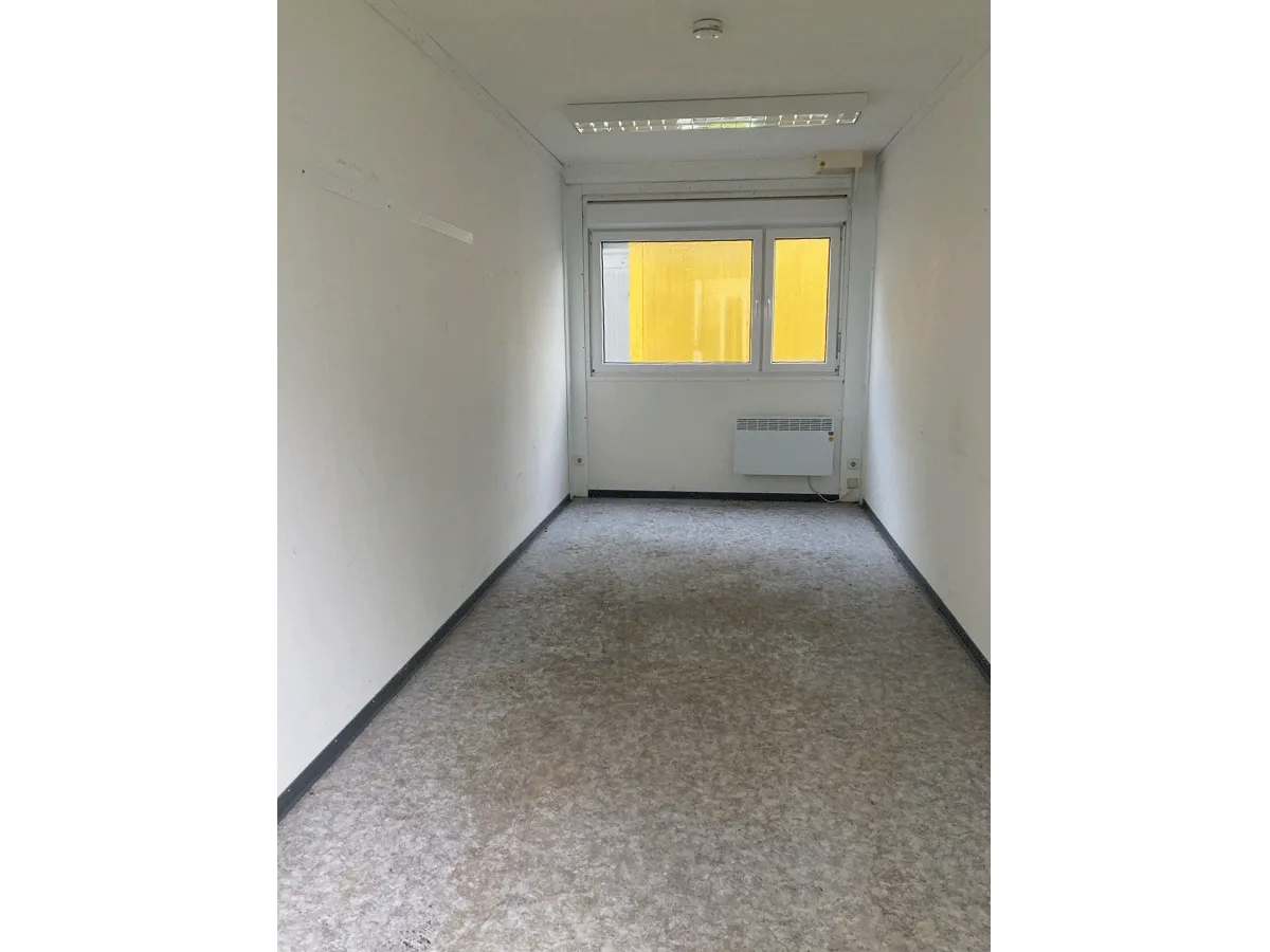 Innenansicht eines grauen Bürocontainers mit geöffnetem Fenster, Elektro-Heizkörper und hellem Bodenbelag.