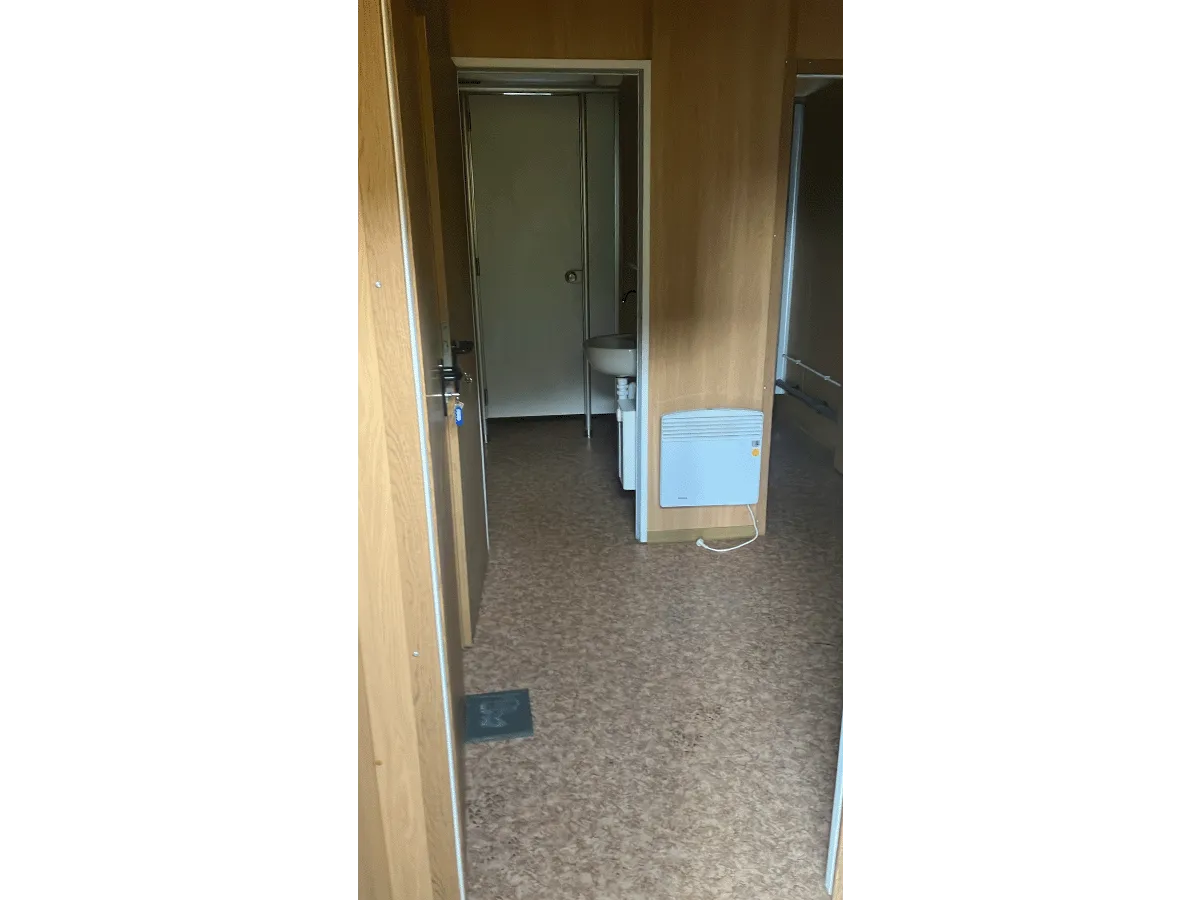 Flur im Container-Innenraum mit Holzwänden, Linoleumboden und Elektroheizkörper