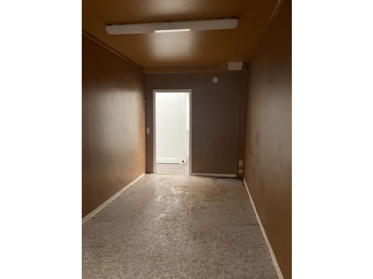 Gebrauchter 20 Fuß Bürocontainer Innenansicht mit Eingangstür, Neonbeleuchtung und Bewegungsmelder – Blick zum Ausgang