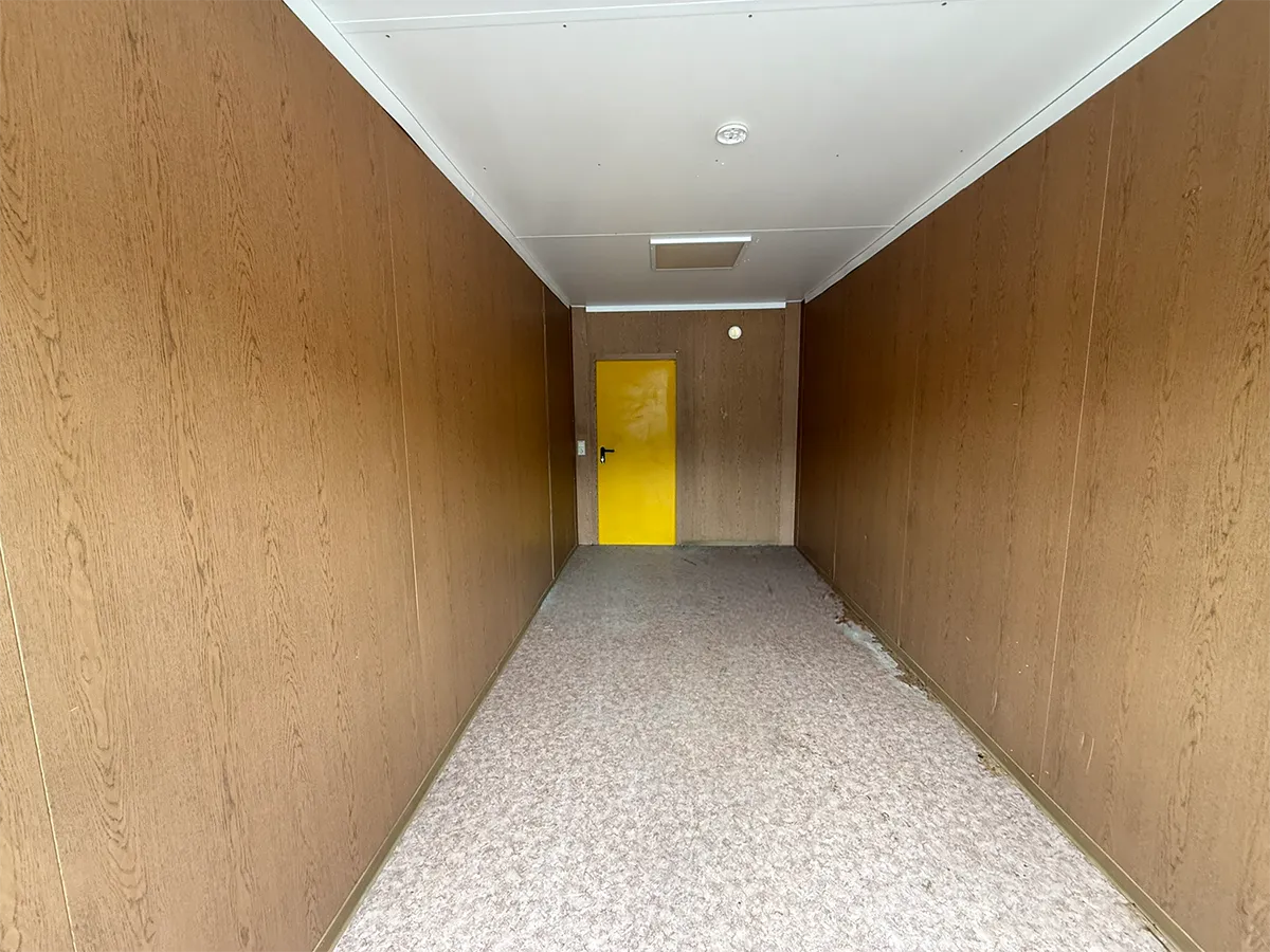 Gebrauchter Bürocontainer Innenansicht mit Holzpaneelen und Blick auf die gelbe Tür