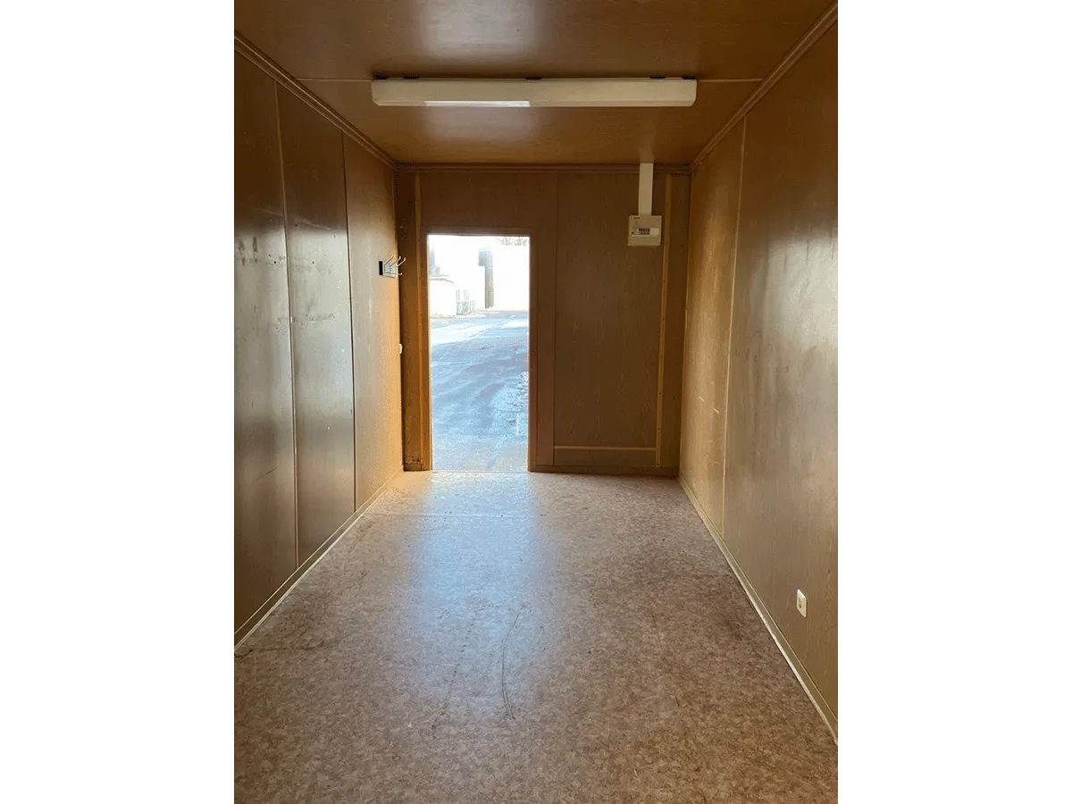 Innenansicht eines gelben Bürocontainers mit Blick auf die geschlossene Eingangstür und die Deckenbeleuchtung.