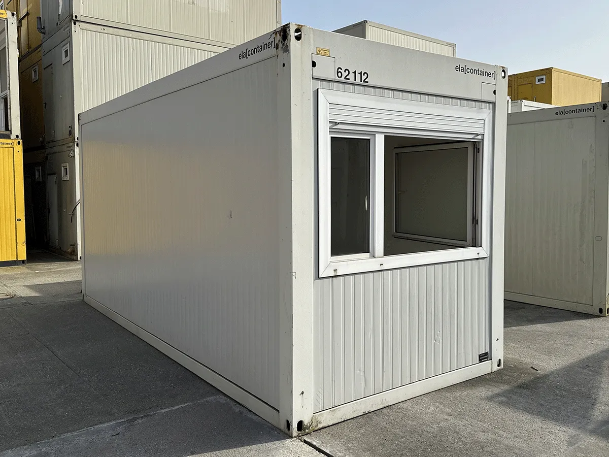 Außenansicht eines gebrauchten grauen Bürocontainers mit Fenster und Rollladen auf einem Lagerplatz.