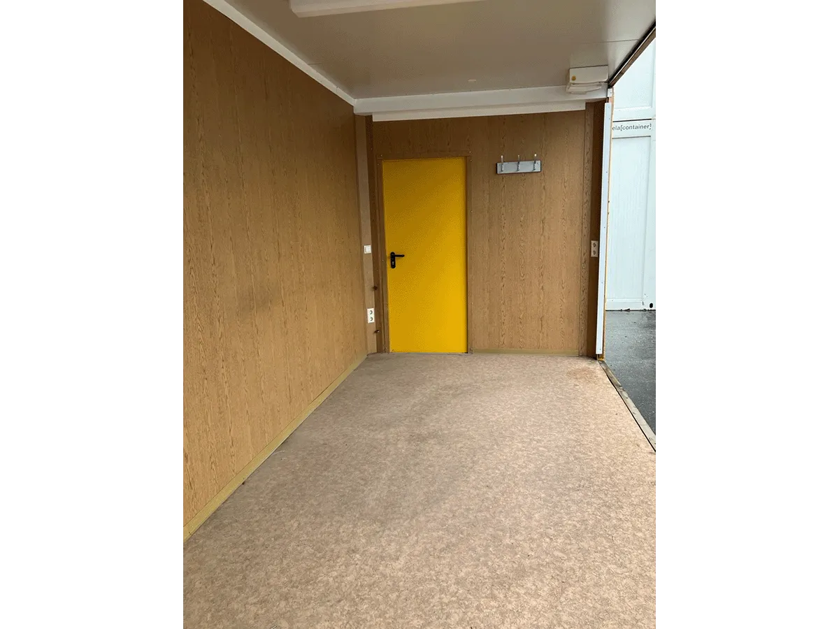 Gebrauchter Bürocontainer Innenraum mit Holzpaneelen gelber Tür und Teppichboden