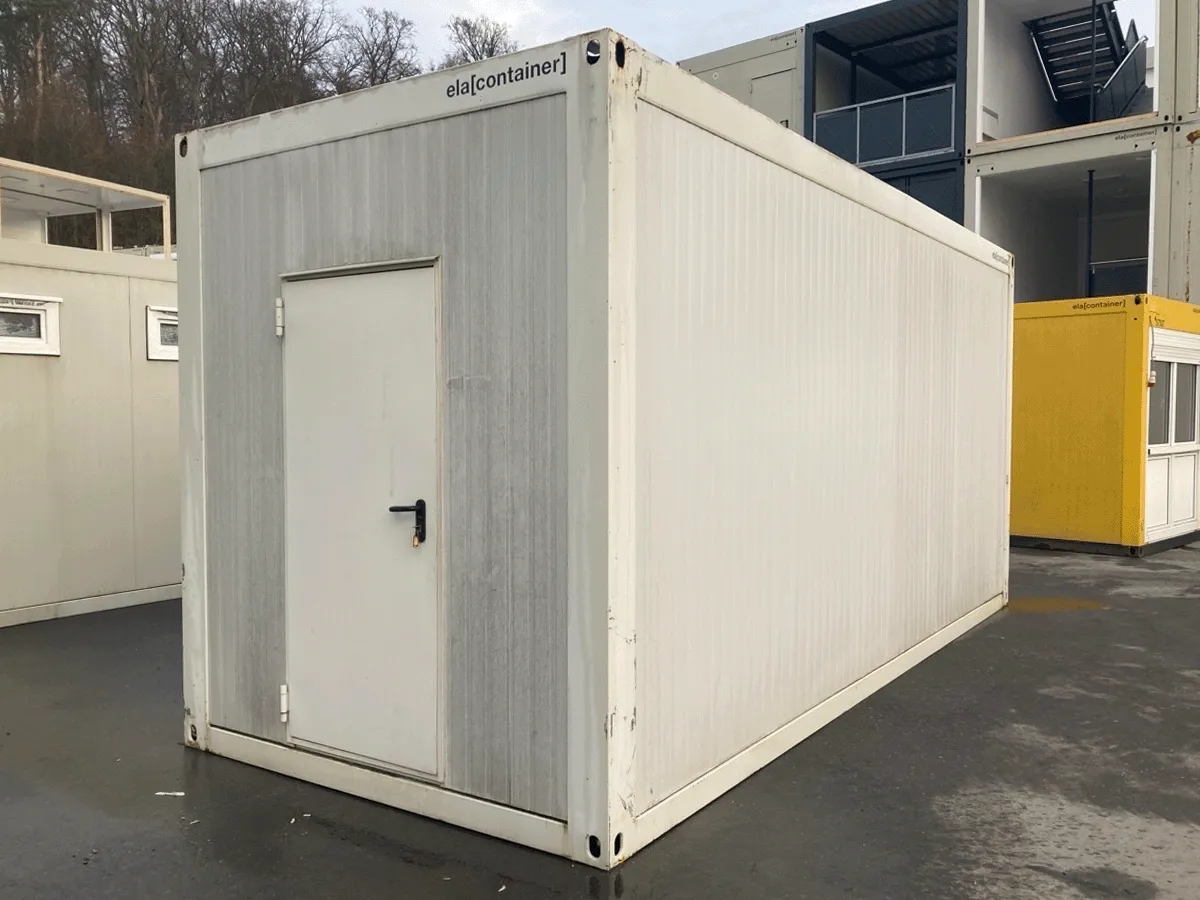 Außenansicht eines gebrauchten grauen Bürocontainers mit Fenster und Rollladen auf einem Lagerplatz.