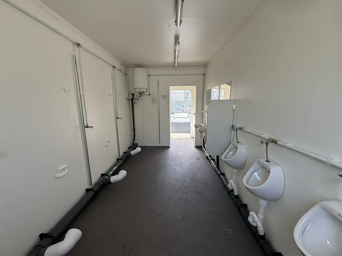 Gebrauchter Sanitärcontainer Innenansicht mit Urinalen und Waschbecken entlang der Wand