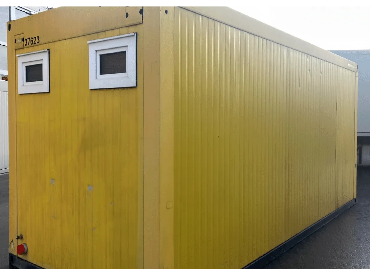 Rückseite eines gelben Sanitärcontainers mit zwei kleinen weißen Fenstern und Metallfassade