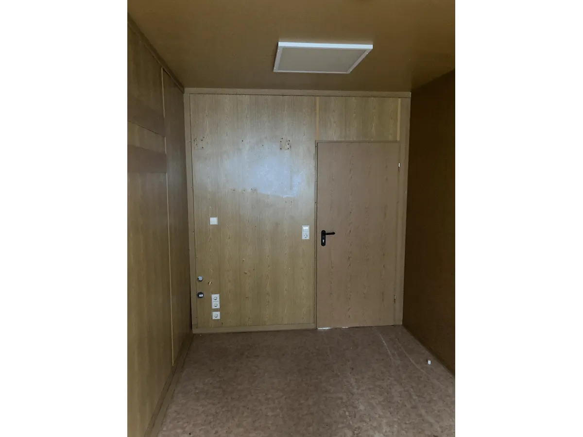 Gebrauchter 20 Fuß Bürocontainer Innenansicht mit Eingangstür, Steckdosen, Deckenleuchte und OSB-Wandverkleidung – Blick auf Türseite"