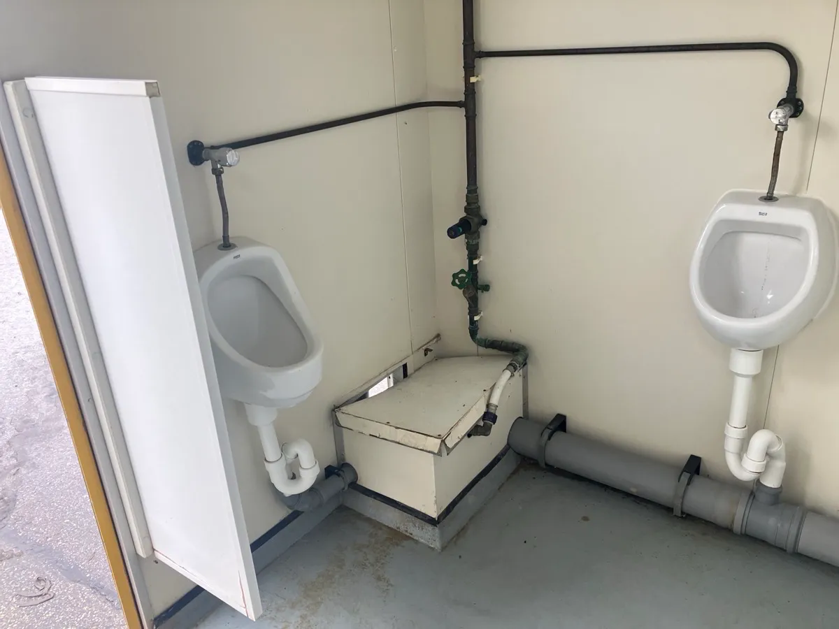 Urinale im Sanitärcontainer mit sichtbaren Leitungen