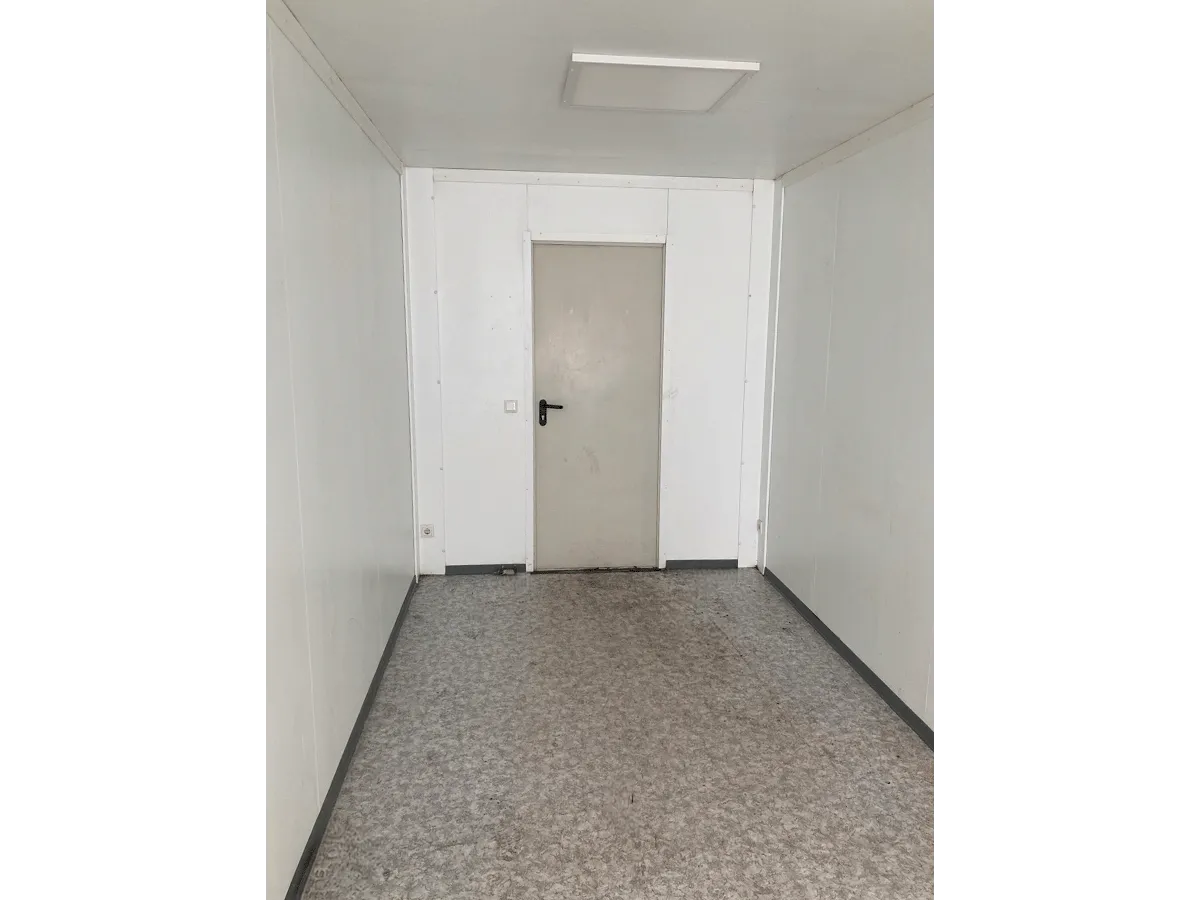 Innenansicht eines leeren grauen Bürocontainers mit Blick auf die geschlossene Innentür.