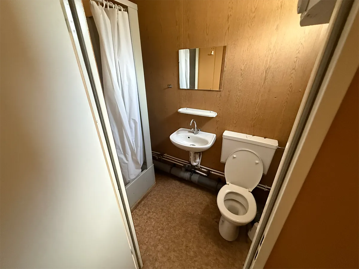 Gebrauchter Bürocontainer Innenansicht mit WC, Waschbecken, Spiegel und Duschvorhang