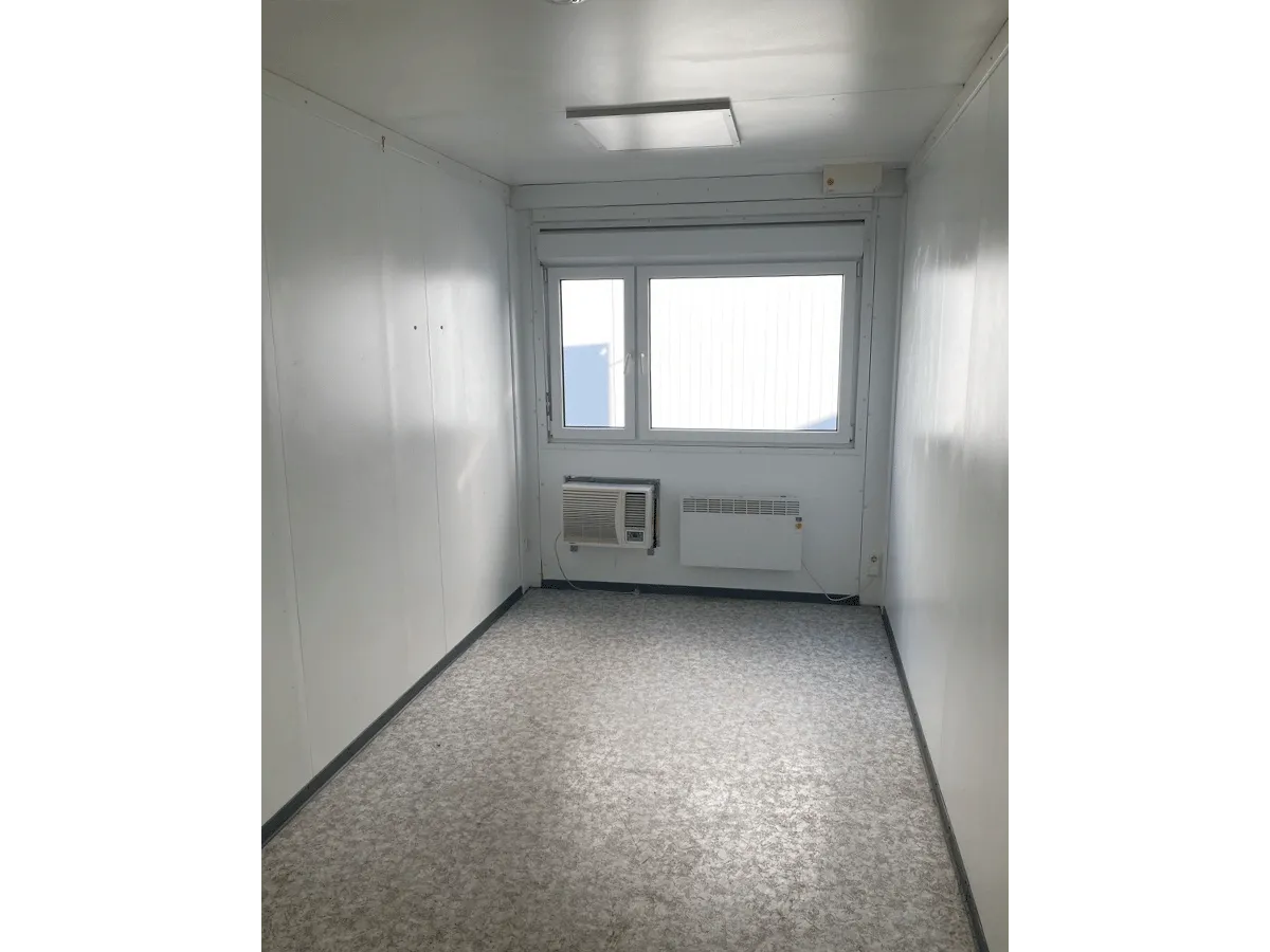 Innenansicht eines grauen Bürocontainers mit Fenster, Heizung, Klimaanlage und Deckenbeleuchtung.