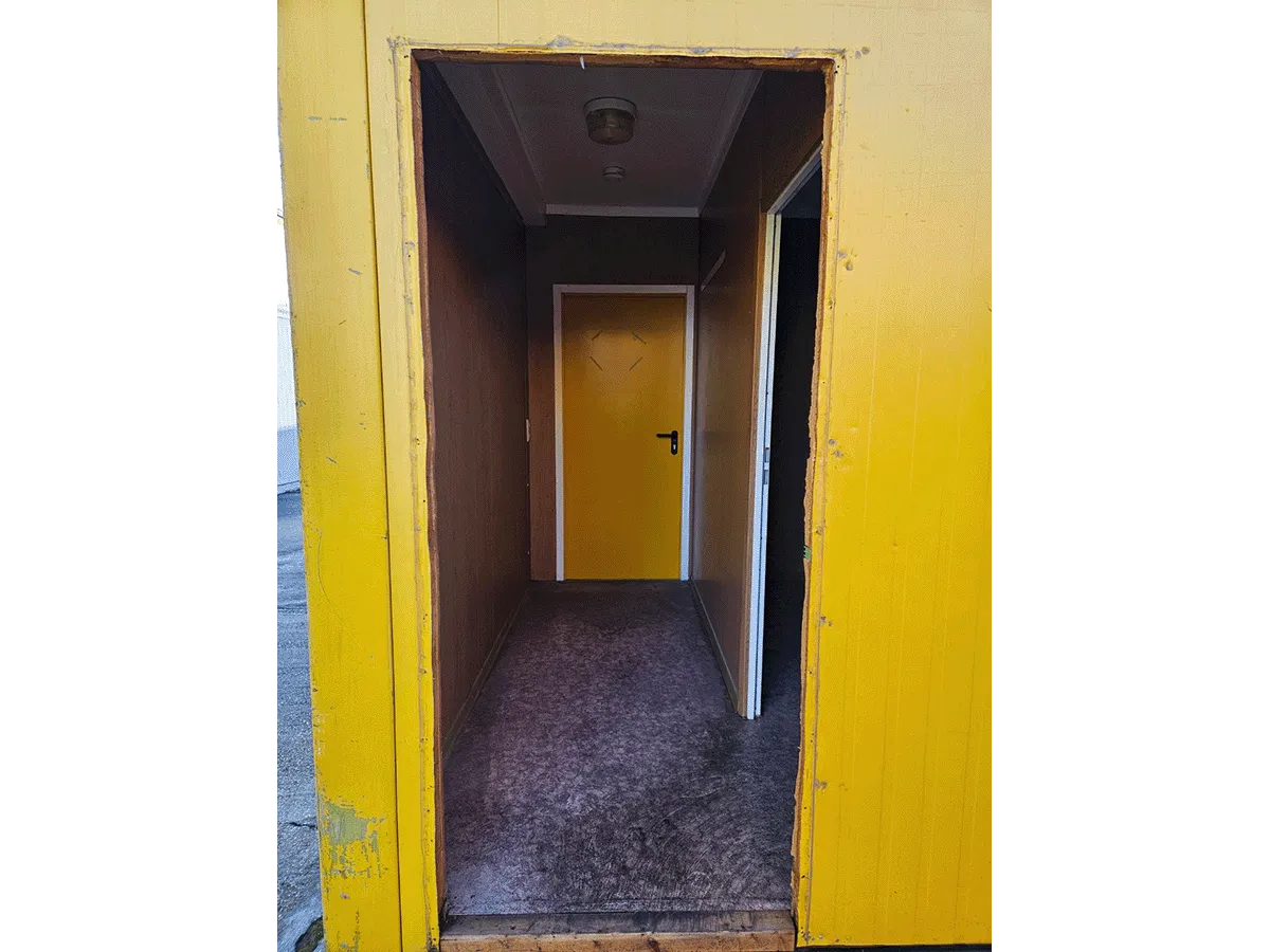Innenansicht des leeren, gelben 20-Fuß-Bürocontainers (3m Breite) mit Blick auf das Doppel-Fenster, Heizkörper und hellem Bodenbelag.