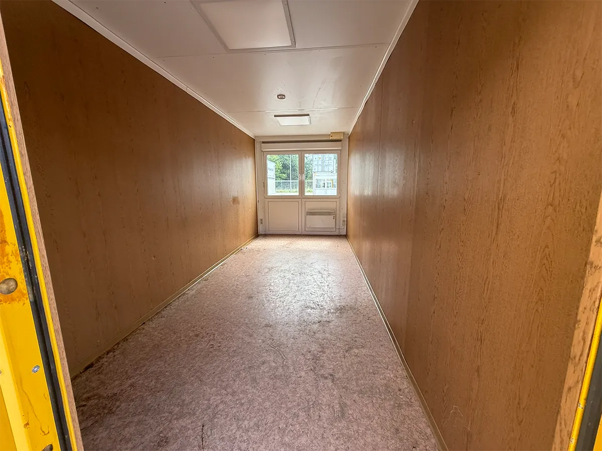Gebrauchter Bürocontainer Innenansicht mit Holzpaneelen, Steinteppichboden und Fenstern