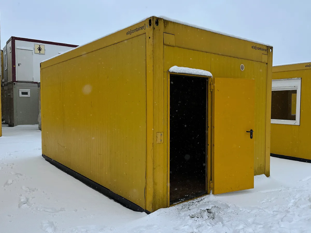 Gebrauchter 20 Fuß Bürocontainer gelb von ELA Container mit offener Eingangstür – Rückansicht im Schnee auf dem Containerplatz