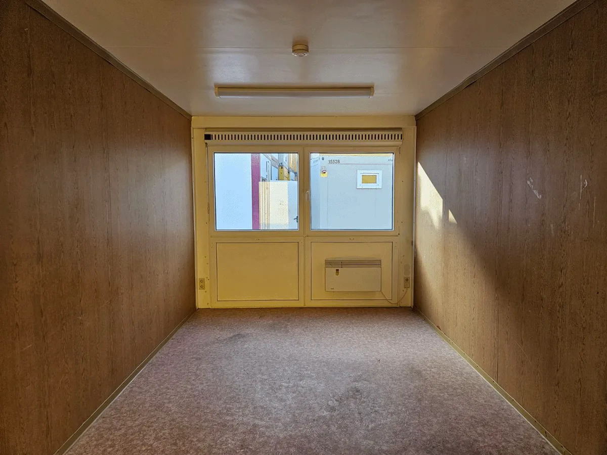 Innenansicht eines leeren gelben Bürocontainers (3m Breite) mit Fenster, Heizung und hellem Bodenbelag.