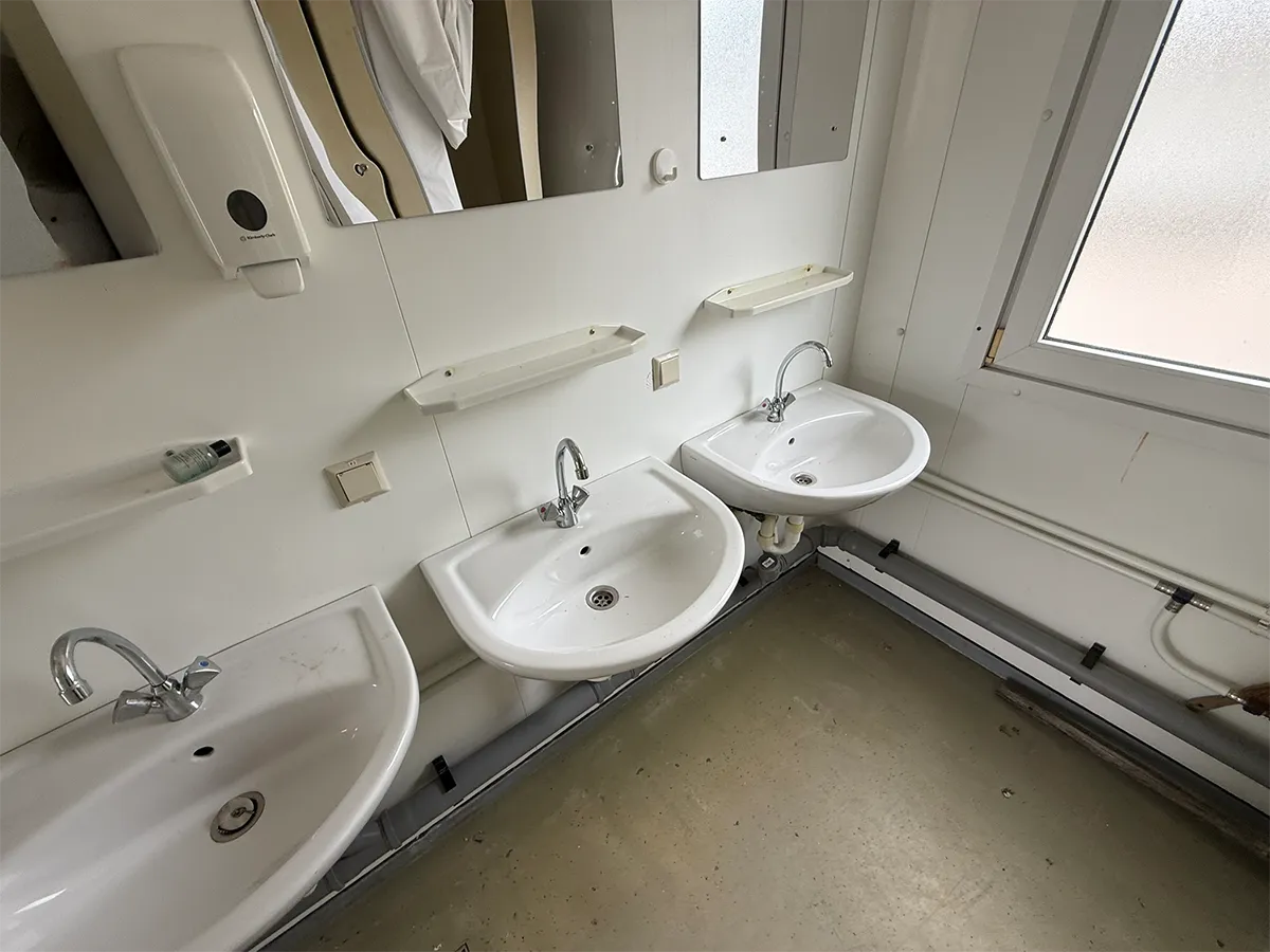 Gebrauchter Sanitärcontainer Innenansicht mit drei Waschbecken und Fenster