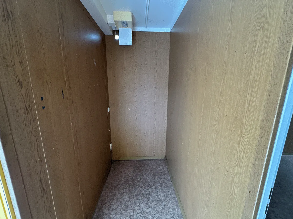 Innenansicht des gelben Bürocontainers mit Blick auf die weiße Eingangstür und die elektrische Deckenbeleuchtung.
