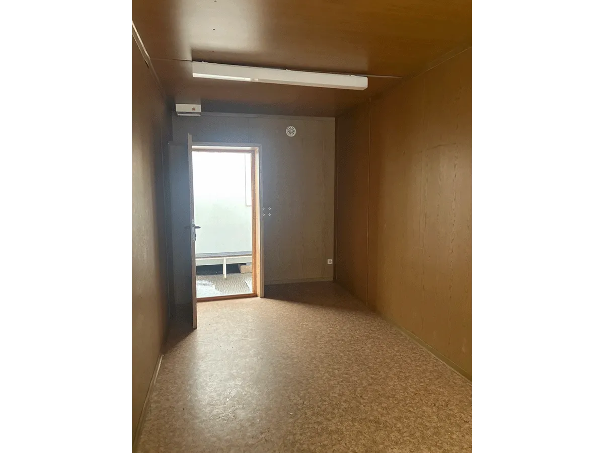 Gebrauchter 20 Fuß Bürocontainer Innenansicht mit offener Eingangstür, Neonbeleuchtung und Bewegungsmelder – Blick zum Ausgang