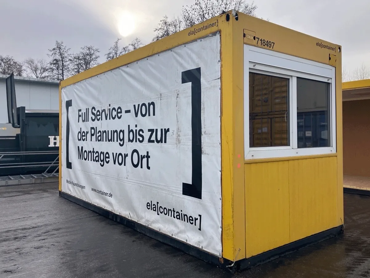 Gebrauchter 20 Fuß Bürocontainer gelb von ELA Container mit Fenster und Werbebanner – Frontansicht auf dem Containerplatz