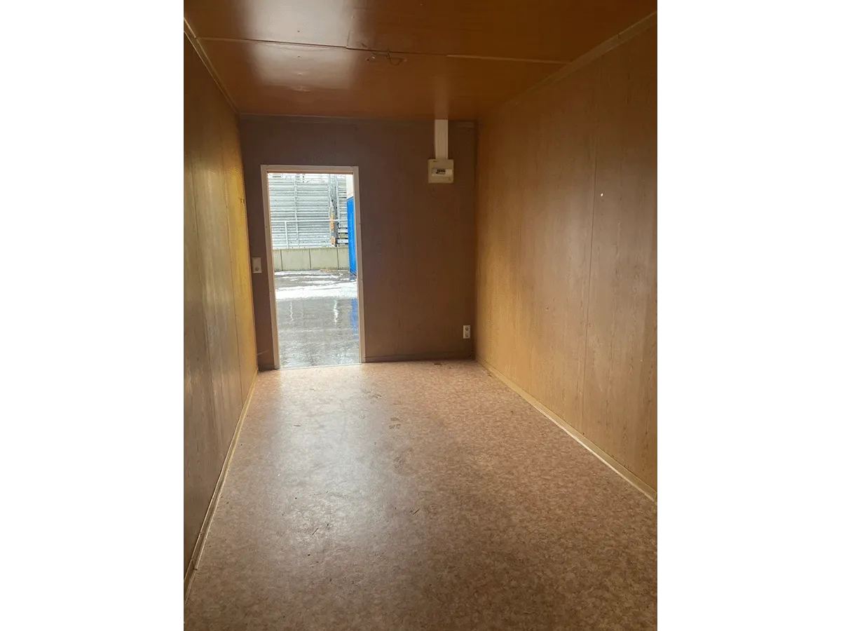 Innenansicht des gelben Bürocontainers mit Blick auf die geschlossene weiße Eingangstür und die Deckenbeleuchtung.