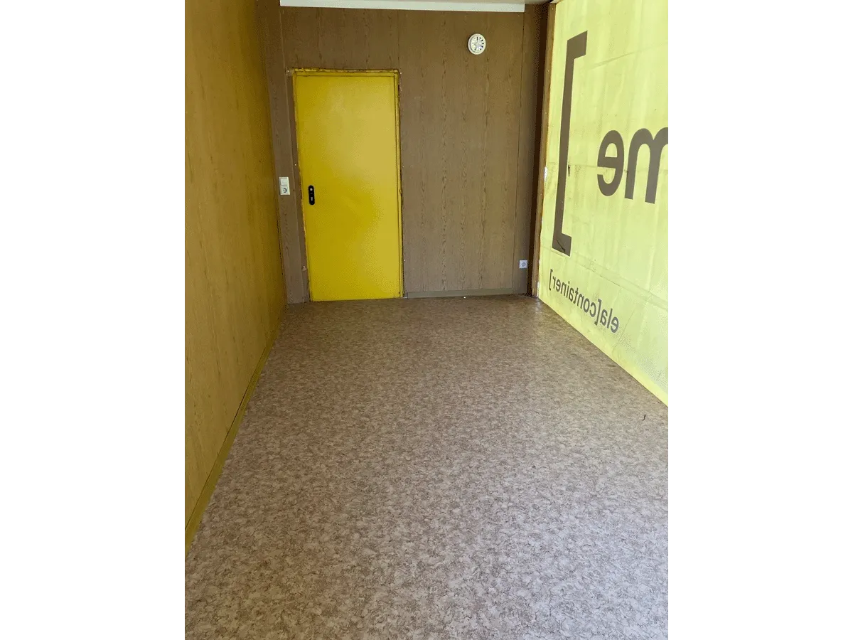 Gebrauchter 20 Fuß Bürocontainer Innenansicht mit gelber Eingangstür, Bewegungsmelder und Vinylboden – Blick zur Türseite