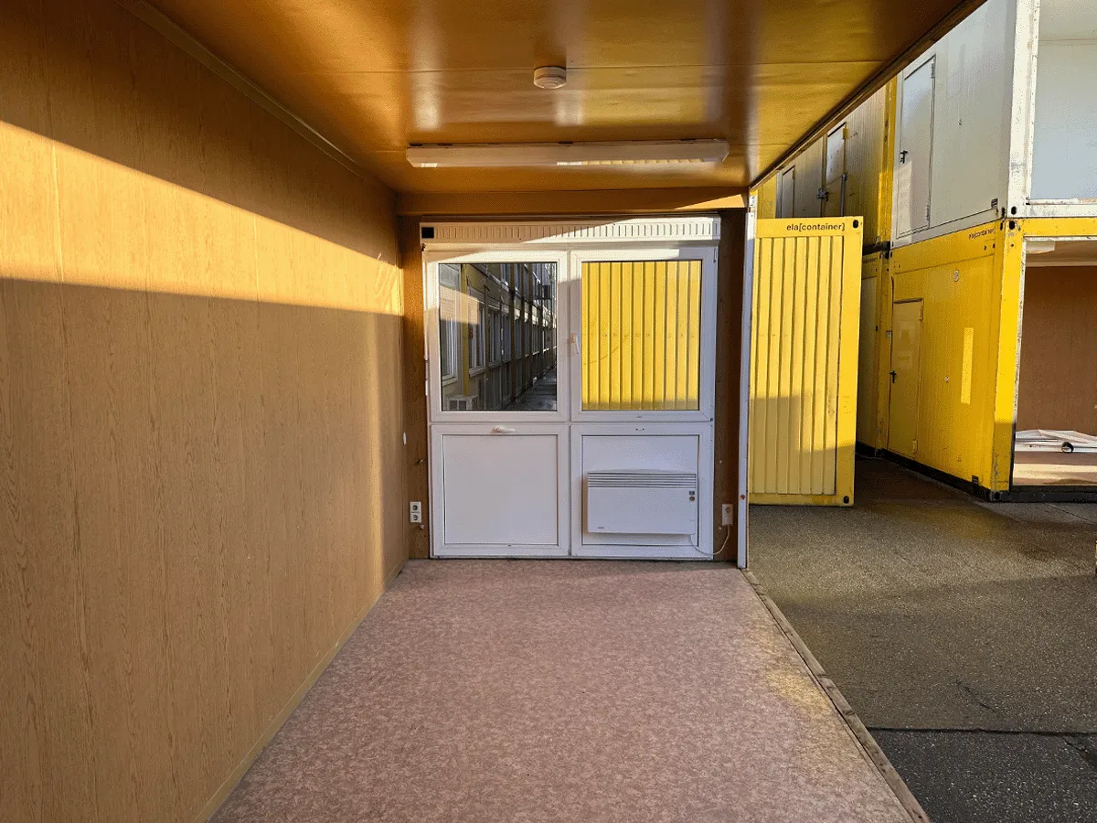 Gebrauchter 20 Fuß Bürocontainer Innenansicht mit Glastür, Heizkörper und OSB-Wandverkleidung – Blick Richtung Eingang