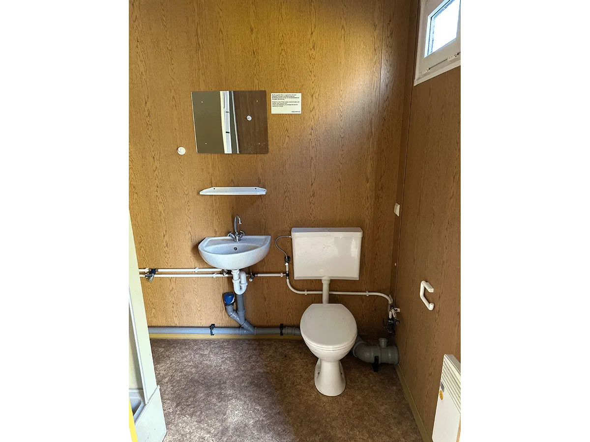 Innenansicht eines leeren gelben Bürocontainers mit Blick auf die Fensterseite und den Heizkörper.