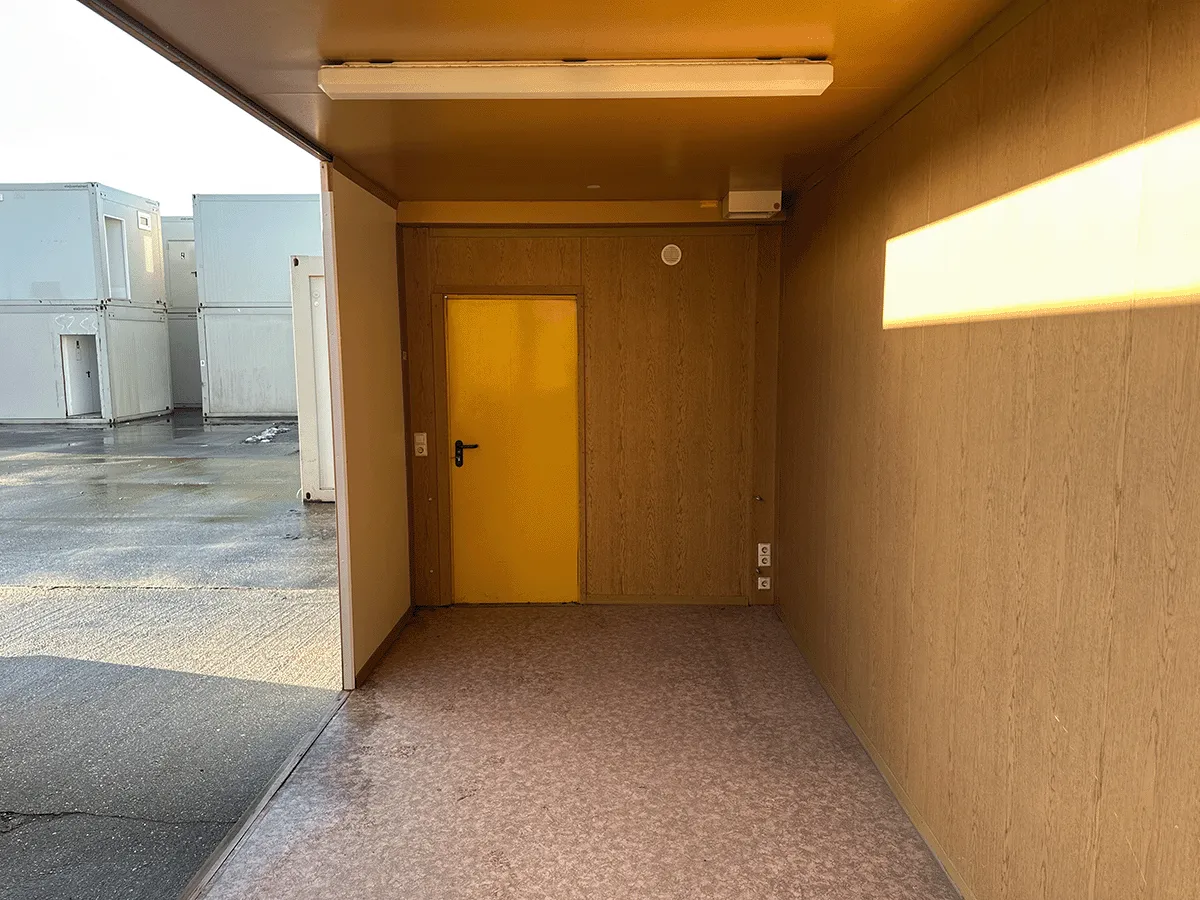 Gebrauchter 20 Fuß Bürocontainer Innenansicht mit gelber Tür, Neonbeleuchtung und Bewegungsmelder – Blick zur Türseite