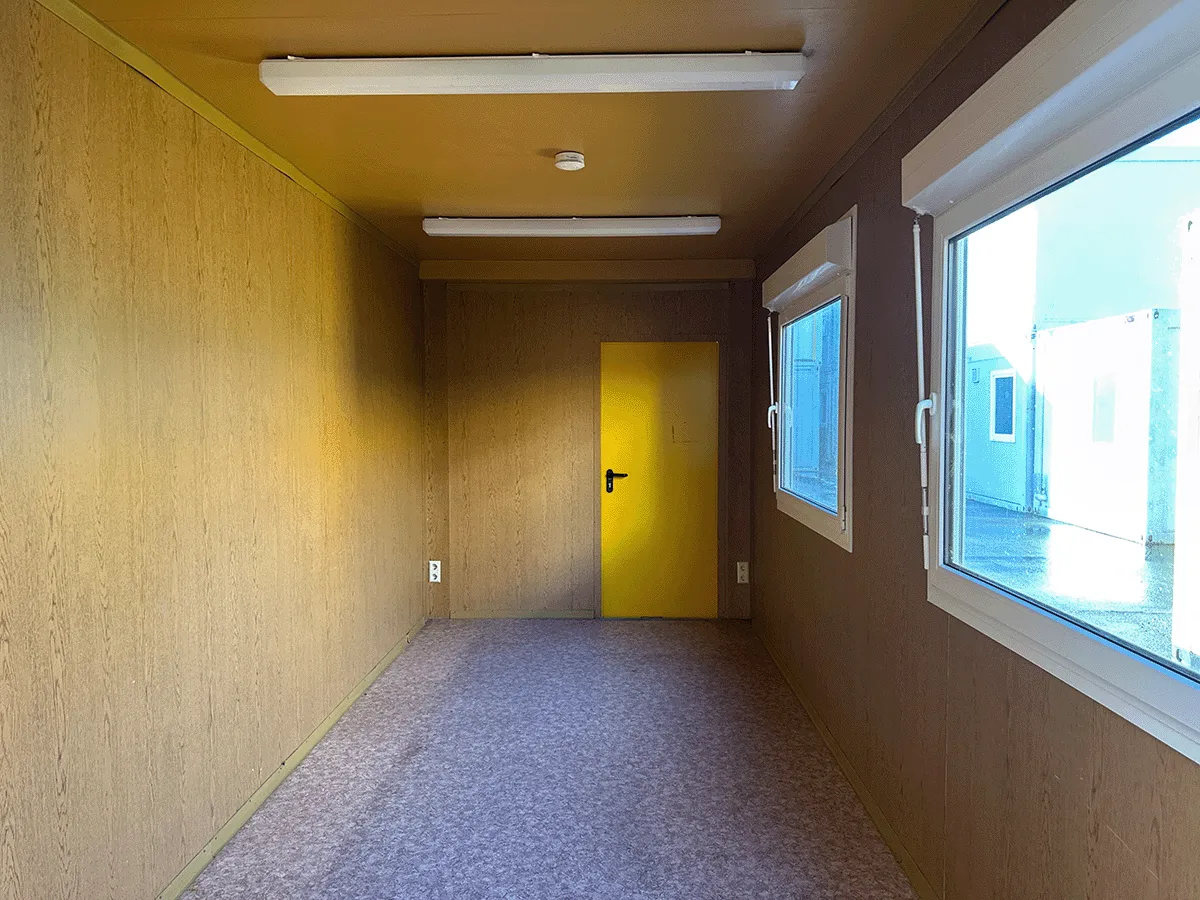 Gebrauchter 20 Fuß Bürocontainer Innenansicht mit gelber Tür, großem Fenster und Neonbeleuchtung – Blick zur Türseite