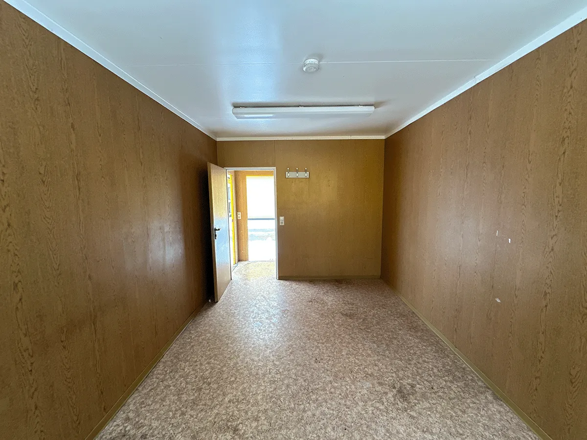 Innenansicht des leeren gelben Bürocontainers (3m Breite) mit Blick auf das Fenster und den Heizkörper.