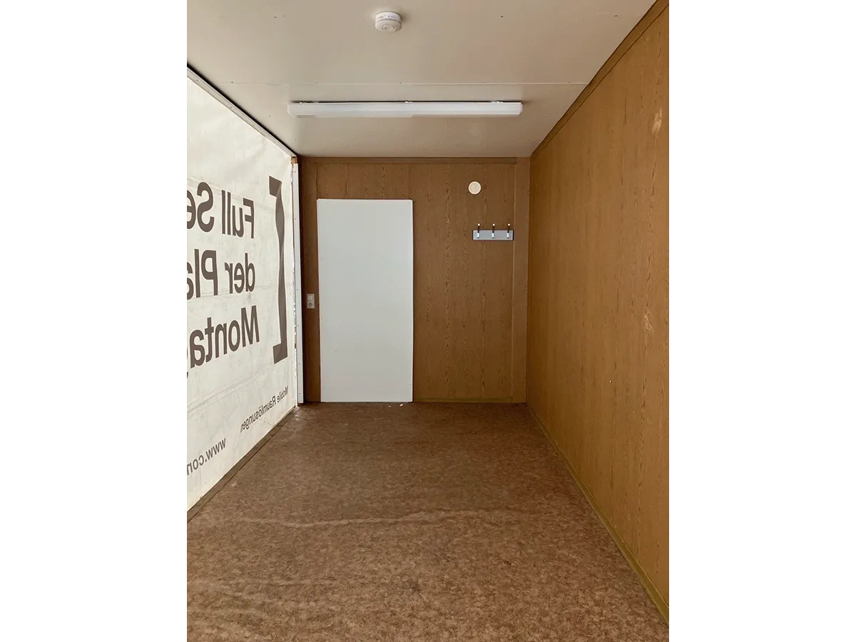 Gebrauchter 20 Fuß Bürocontainer Innenansicht mit Eingangstür, Bewegungsmelder und Neonbeleuchtung – Blick zur Türseite