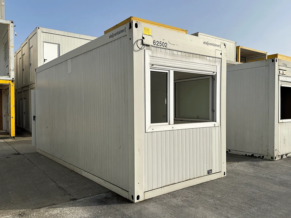Außenansicht eines gebrauchten grauen Bürocontainers mit Fenster und Rollladen auf einem asphaltierten Platz.