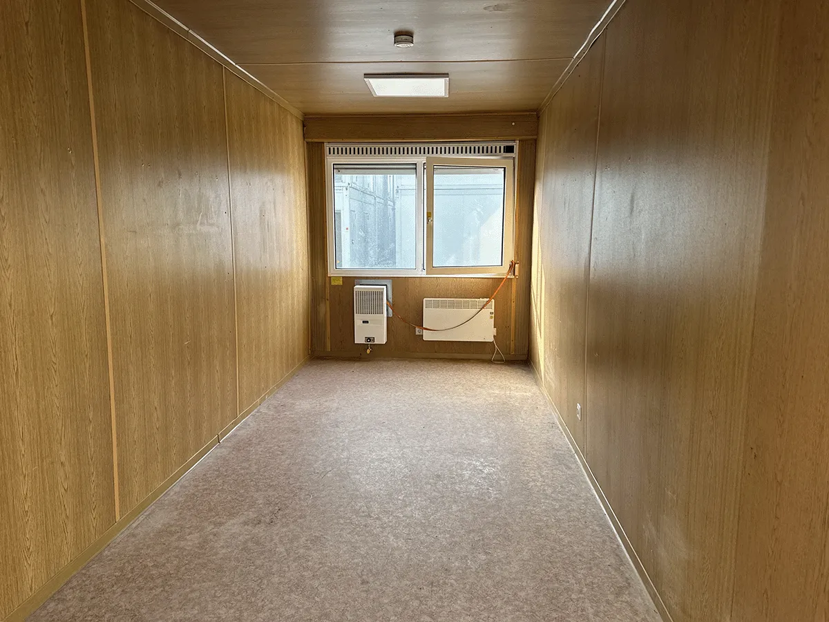 Innenansicht eines leeren grauen 20-Fuß-Bürocontainers mit Blick auf das Doppel-Schiebefenster und den Heizkörper.