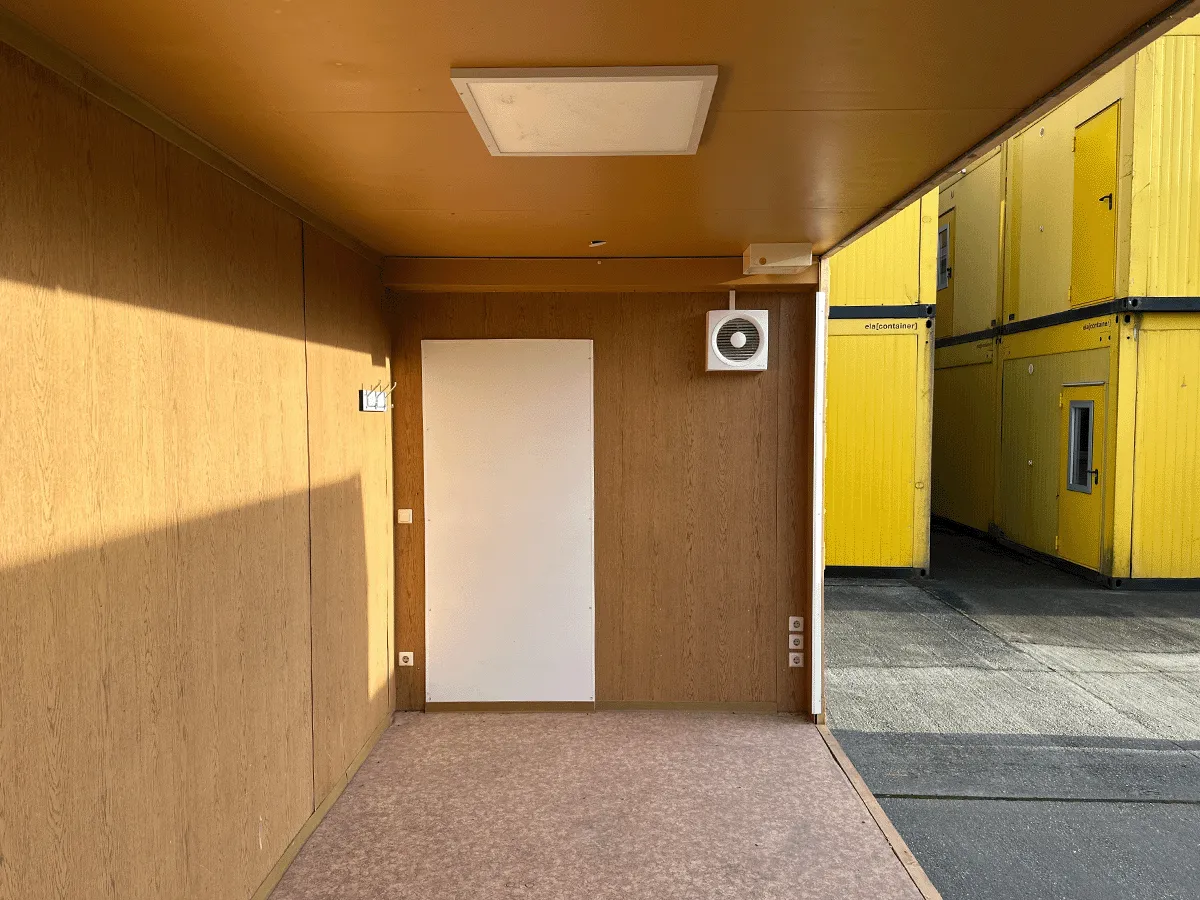 Gebrauchter 20 Fuß Bürocontainer Innenansicht mit Eingangstür, Lüftung und Deckenleuchte – Blick zur Türseite mit offener Seitenfront