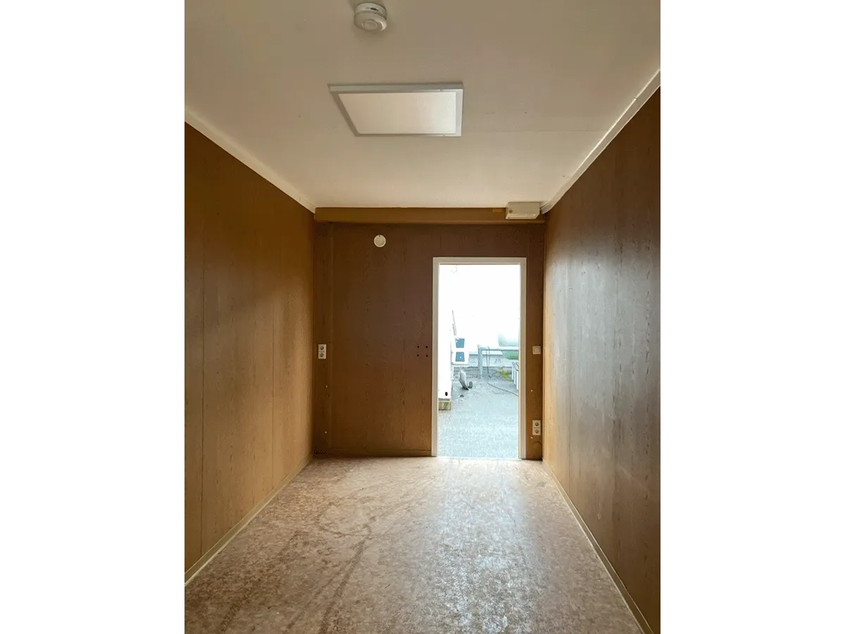 Gebrauchter 20 Fuß Bürocontainer Innenansicht mit offener Eingangstür, Steckdosen und Bewegungsmelder – Blick zum Ausgang