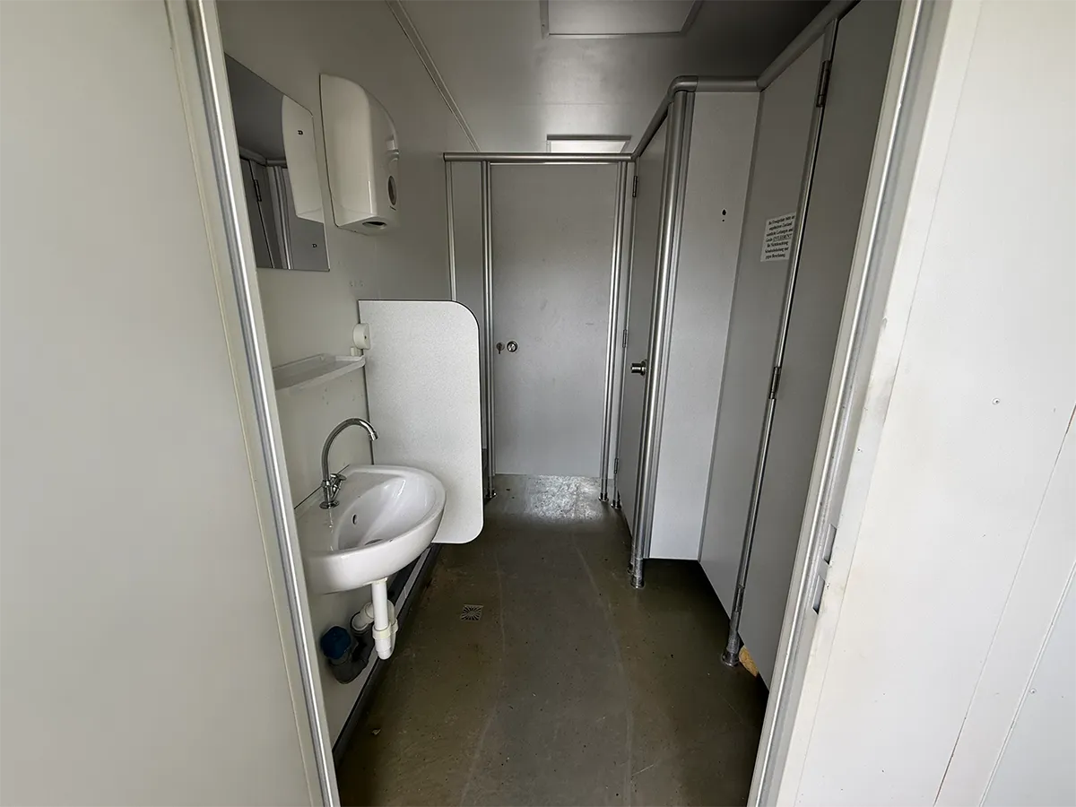 Gebrauchter Sanitärcontainer Innenansicht mit Waschbecken und Kabinentüren